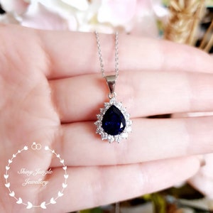 Puede incluir: Un collar de plata con un colgante de zafiro azul en forma de pera rodeado por un halo de piedras transparentes m&aacute;s peque&ntilde;as.