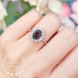May include: A silver ring with a large oval-shaped red gemstone surrounded by smaller white gemstones.
