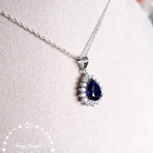 Puede incluir: Un collar de plata con un colgante en forma de l&aacute;grima que presenta una gran piedra azul rodeada de piedras transparentes m&aacute;s peque&ntilde;as.