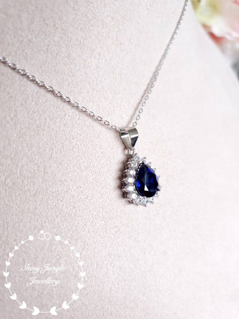 Puede incluir: Un collar de plata con un colgante en forma de l&aacute;grima que presenta una gran piedra azul rodeada de piedras transparentes m&aacute;s peque&ntilde;as.