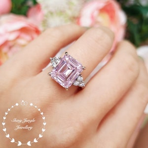 Pu&ograve; includere: Un anello di fidanzamento in argento con un grande diamante rosa a taglio smeraldo e diamanti pi&ugrave; piccoli sulla fascia.