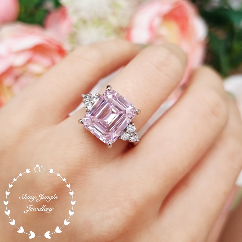 Pu&ograve; includere: Un anello di fidanzamento in argento con un grande diamante rosa a taglio smeraldo e diamanti pi&ugrave; piccoli sulla fascia.