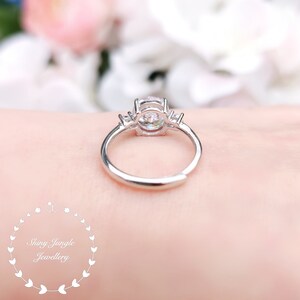 May include: A silver ring with a large round clear stone and two smaller clear stones on either side. The ring is on a person's finger.