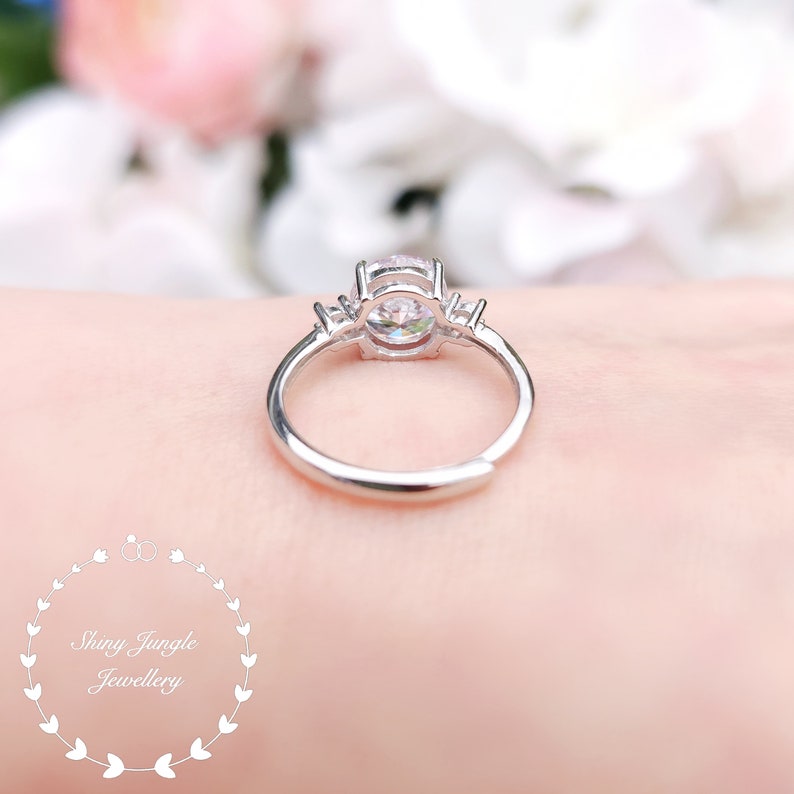 May include: A silver ring with a large round clear stone and two smaller clear stones on either side. The ring is on a person's finger.