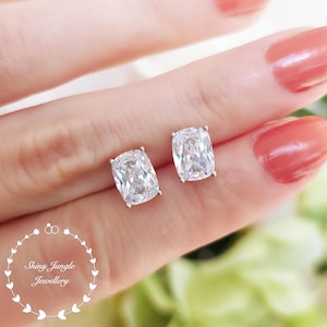 May include: A pair of silver stud earrings with large, clear, cushion-cut cubic zirconia stones.