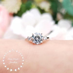 May include: A silver ring with a large, round, clear center stone and two smaller, round, clear stones on either side.