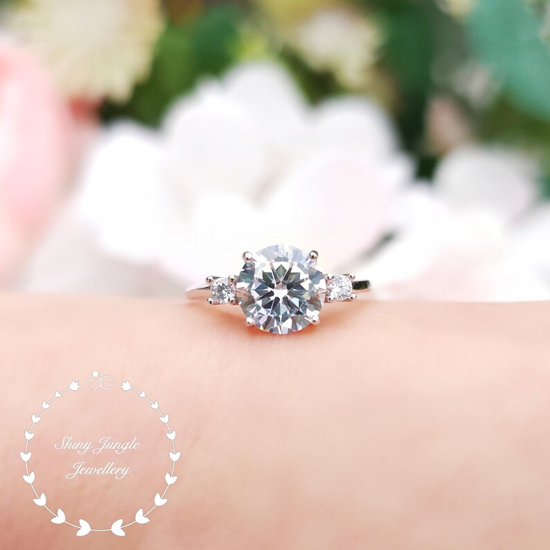 May include: A silver ring with a large, round, clear center stone and two smaller, round, clear stones on either side.