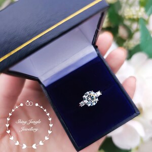 May include: A silver ring with a large round clear stone and two smaller clear stones on the band. The ring is in a blue velvet ring box.