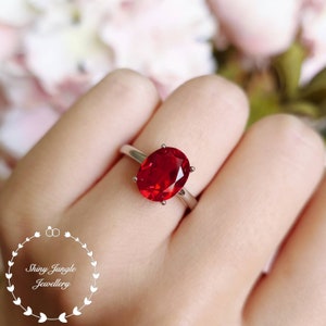 May include: A silver ring with a large, oval-shaped, red gemstone.