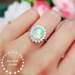 Könnte beinhalten: Ein silberner Ring mit einem großen ovalen Opal-Edelstein, der von kleineren klaren Zirkonia-Steinen umgeben ist.