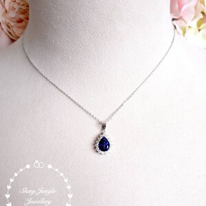 Puede incluir: Un collar de plata con un colgante en forma de l&aacute;grima que presenta una piedra preciosa azul oscuro rodeada de piedras preciosas transparentes m&aacute;s peque&ntilde;as.