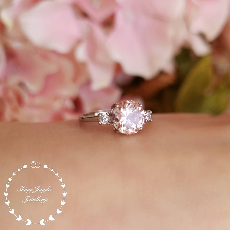 May include: A silver ring with a large, round, pale pink gemstone surrounded by three smaller, round, clear gemstones.