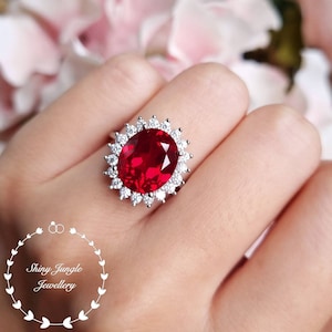 May include: A silver ring with a large oval-shaped red gemstone surrounded by smaller clear gemstones.