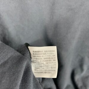Pu&ograve; includere: Primo piano di un tessuto grigio scuro con un'etichetta bianca attaccata. L'etichetta contiene testo giapponese con istruzioni per la cura del lavaggio e dell'asciugatura del tessuto. Il tessuto sembra essere un materiale morbido e tessuto.