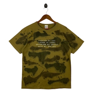 May include: Olive green t-shirt with a camouflage pattern in shades of green and brown. The shirt features the text "Fighter by Day, Lover by Night, Drunkard by Choice, Army by Mistake" in white lettering. The t-shirt is hanging on a wooden hanger.