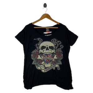 Op de afbeelding: Zwart T-shirt met een schedelontwerp, versierd met een Britse vlag, rozen en wijnranken. De tekst "DEDICATED ENGROSSING" staat op een banner. Het T-shirt hangt aan een houten hanger. Het shirt heeft een distressed look.