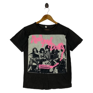 Könnte beinhalten: Schwarzes T-Shirt mit einem rosa-weißen Aufdruck der New York Dolls. Das Bild zeigt die Bandmitglieder im Sitzen. Der Text "New York Dolls" ist in Rosa über dem Bild gedruckt und vermittelt ein Vintage-Rock'n'Roll-Feeling.