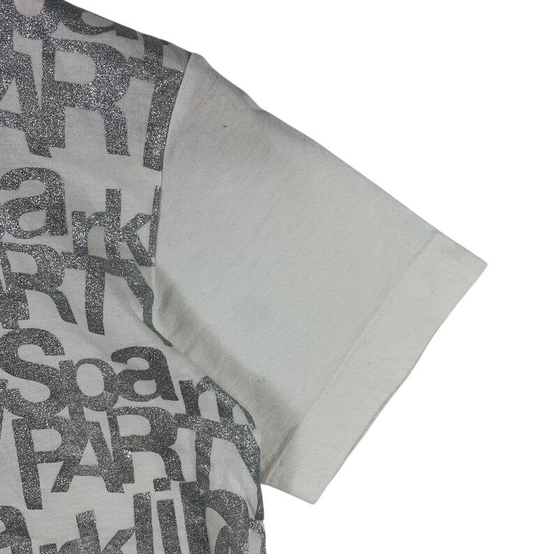 Puede incluir: Camiseta blanca de manga corta. La camiseta tiene un estampado gr&aacute;fico plateado brillante con las palabras "Spark" y "Art" en negrita. Fabricada con un material suave y ligero.
