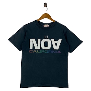Puede incluir: Camiseta negra con la palabra "NOV" en letras blancas grandes y "CALIFORNIA" en colores arcoíris. La camiseta está colgada de una percha de madera.