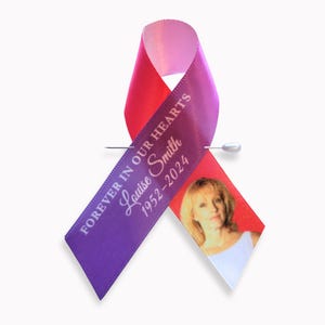 Peut inclure: Un ruban de sensibilisation violet et rose avec un message comm&eacute;moratif imprim&eacute; en blanc indiquant FOREVER IN OUR HEARTS, le nom Louise Smith et les ann&eacute;es 1952-2024. Une petite photo d'une personne est imprim&eacute;e sur le pan droit du ruban.
