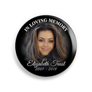 May include: A black and white button with a photo of a young woman and the text "In Loving Memory Elizabeth Trust 2001 - 2018".