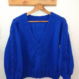 Puede incluir: Un suéter de punto azul real con cuello en V y detalles calados en las mangas y los puños.