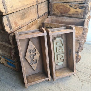 May include: A collection of antique wooden brick moulds. Two moulds are in the foreground, one with a diamond-shaped design and the numbers "252", the other with a decorative pattern. The moulds are various shades of brown.
