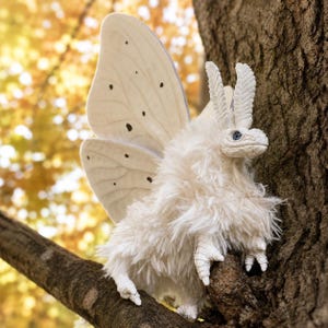 May include: A plush moth figure with a fluffy white body, textured white wings featuring small black spots, and detailed white antennae. The creature has a sculpted head with blue eyes and clawed feet, designed with a soft, shaggy texture.
