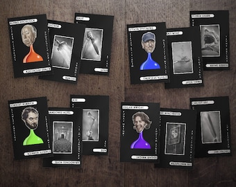 Può includere: Un set di carte nere con illustrazioni e nomi di famosi registi e immagini legate al cinema. Le carte presentano immagini di Alfred Hitchcock, Stanley Kubrick, Steven Spielberg ed Edgar Wright, insieme a immagini di una doccia, un coltello, un'ascia e altro.