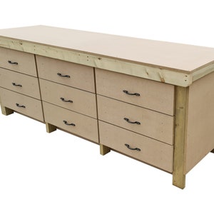 May include: A large wooden workbench with a light brown top and eight drawers. The drawers have black metal handles. The workbench is made of unfinished wood.
