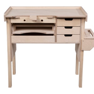 May include: A light wood workbench with three drawers and a side shelf. The workbench has a top surface with a small ledge and a few holes. The workbench is on four legs.