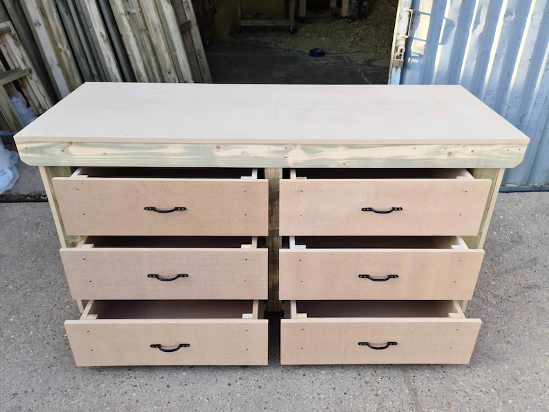 May include: A wooden workbench with six drawers. The drawers are open and have black metal handles. The workbench is made of unfinished wood.