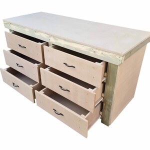 May include: A wooden workbench with a light brown top and six drawers. The drawers are open and reveal a light brown interior. The workbench is made of wood and has a rustic look.