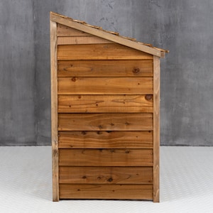 May include: A wooden dog house with a slanted roof. The house is made of brown wood planks and has a natural wood finish.