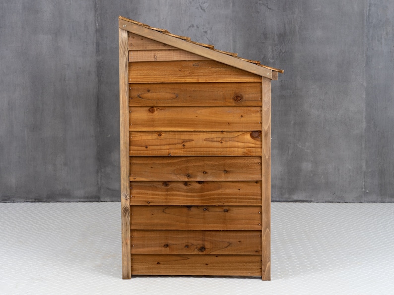 May include: A wooden dog house with a slanted roof. The house is made of brown wood planks and has a natural wood finish.