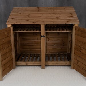 May include: A wooden log storage shed with two doors open, revealing two compartments with slatted shelves. The shed has a brown stain finish and a pitched roof.