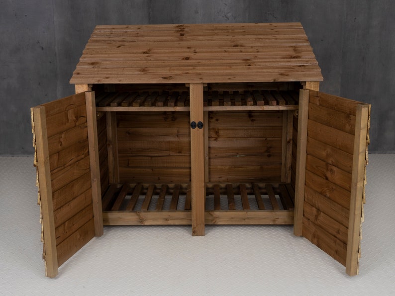 May include: A wooden log storage shed with two doors open, revealing two compartments with slatted shelves. The shed has a brown stain finish and a pitched roof.