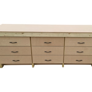 May include: A wooden workbench with nine drawers and black metal handles. The workbench is made of light wood and has a natural finish.