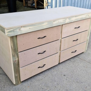 May include: A wooden workbench with six drawers and black metal handles. The workbench has a light wood top and a dark wood base.