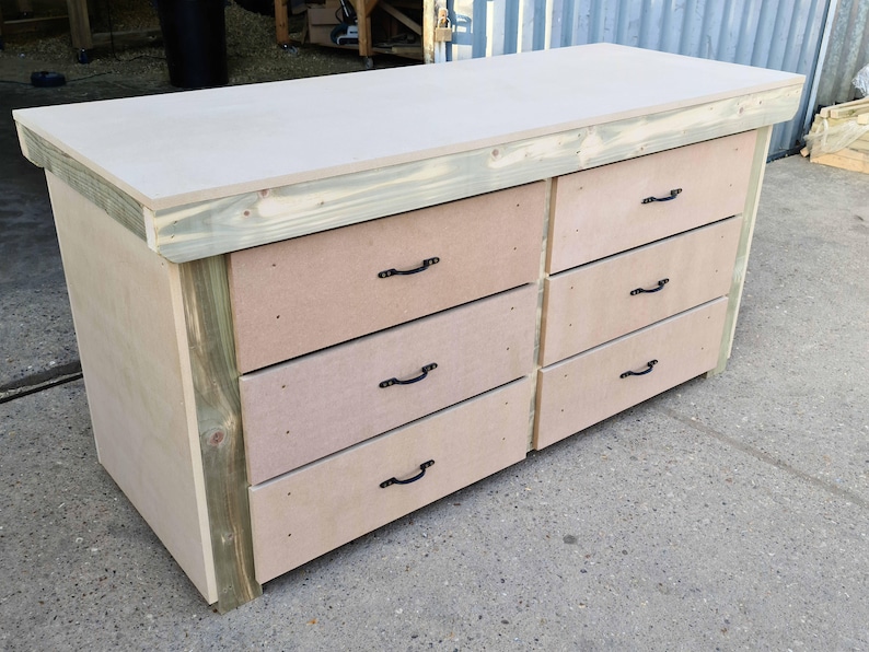 May include: A wooden workbench with six drawers and black metal handles. The workbench has a light wood top and a dark wood base.