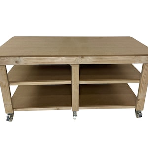May include: A wooden workbench with two shelves and four wheels. The workbench is made of natural wood and has a light brown finish.