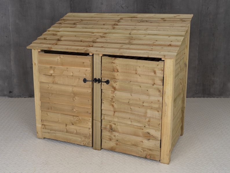 May include: A wooden double-door bin storage unit with a slanted roof. The unit has two doors with black metal latches.
