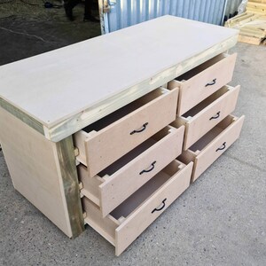 May include: A wooden workbench with a light brown top and six drawers. The drawers have black metal handles and are open to reveal the interior.