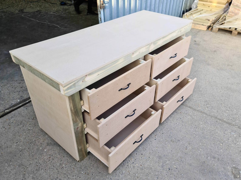 May include: A wooden workbench with a light brown top and six drawers. The drawers have black metal handles and are open to reveal the interior.