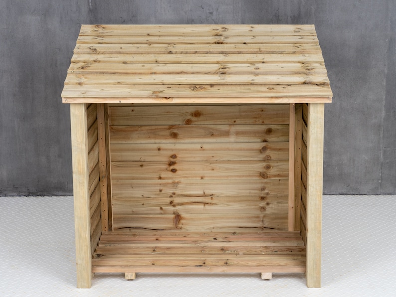 May include: A wooden log storage shed with a slanted roof and a slatted front. The shed is empty and ready to be filled with firewood.
