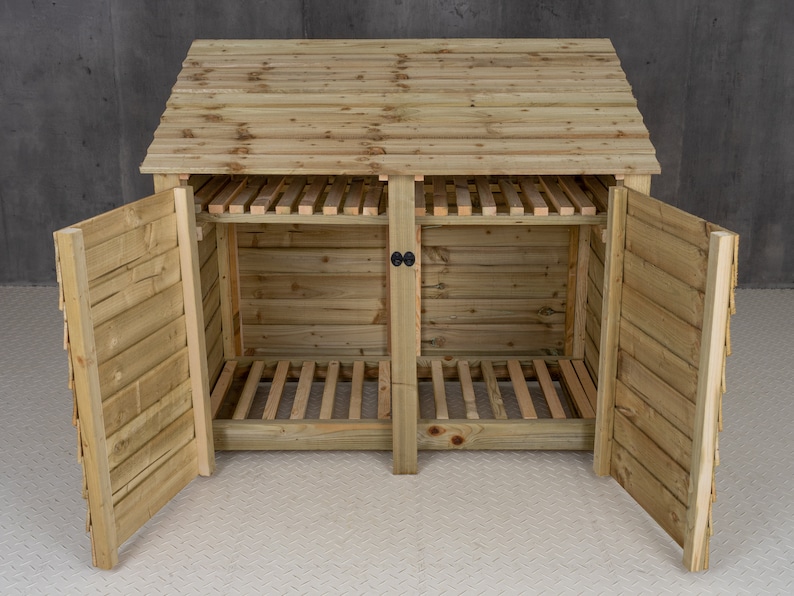 May include: A wooden log storage shed with a gabled roof and two doors. The doors are open, revealing the interior with shelves and a slatted floor.