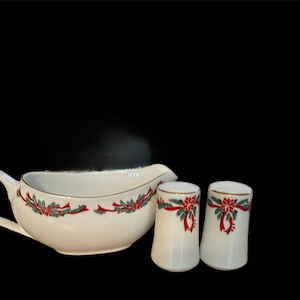 May include: White porcelain gravy boat and two salt and pepper shakers with a Christmas-themed design featuring red bows, green holly leaves, and red poinsettia flowers.