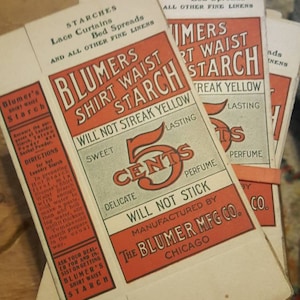 May include: A stack of five-cent packages of Blumer's Shirt Waist Starch, a laundry product. The packages are red, white, and black with the text "Blumer's Shirt Waist Starch" and "Will Not Streak Yellow".
