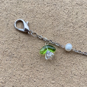 May include: A silver chain necklace with a green glass flower charm and a white pearl charm.