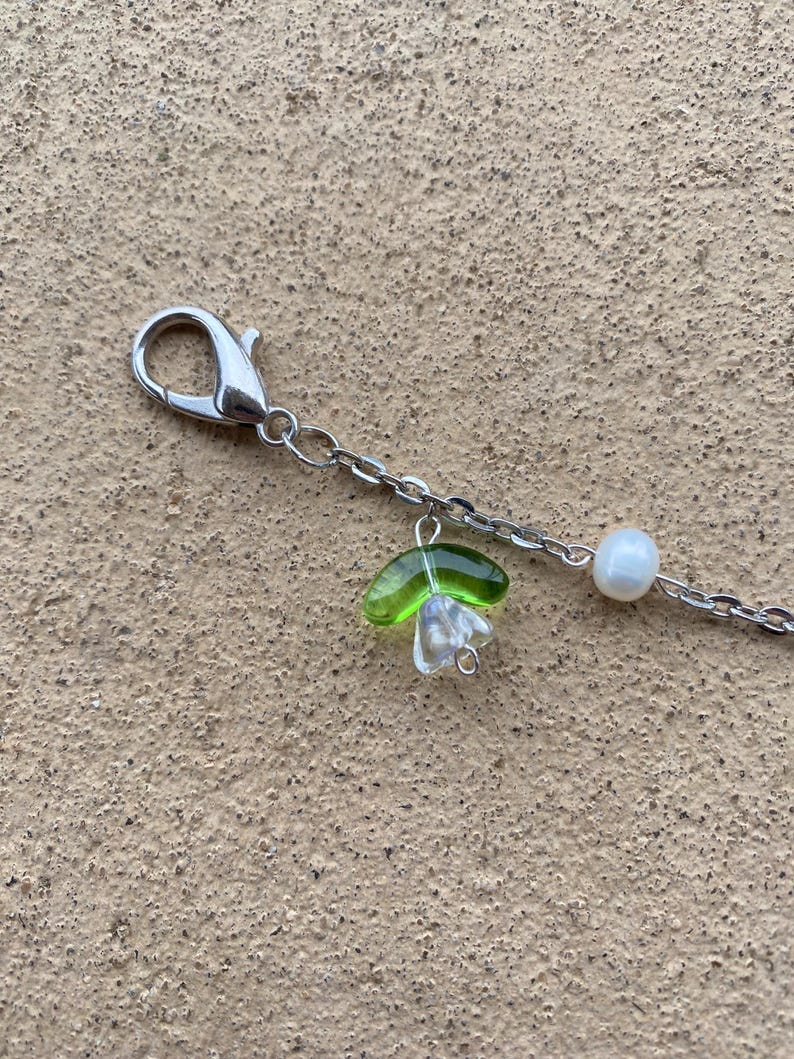 May include: A silver chain necklace with a green glass flower charm and a white pearl charm.
